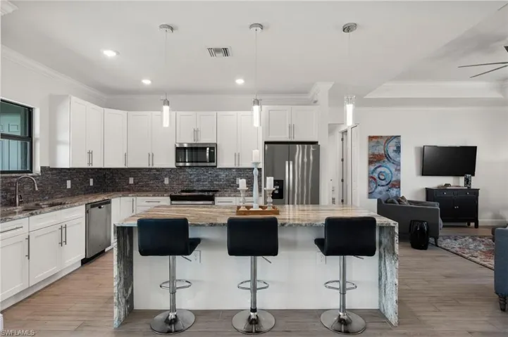 Kitchen featuring light stone counters, backsplash, visible vents, stainless steel appliances, and a sink