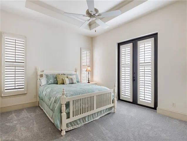 Bedroom with carpet, multiple windows, a raised ceiling, and ceiling fan