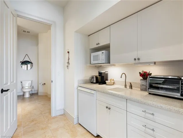 Kitchen featuring light stone counters, white appliances, sink, light tile patterned floors, and white cabinetry