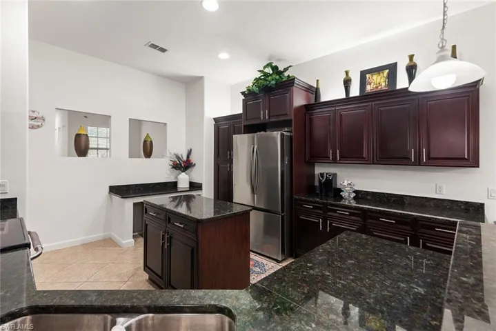 Kitchen featuring freestanding refrigerator, a center island, dark stone counters, hanging light fixtures, and dark brown cabinets