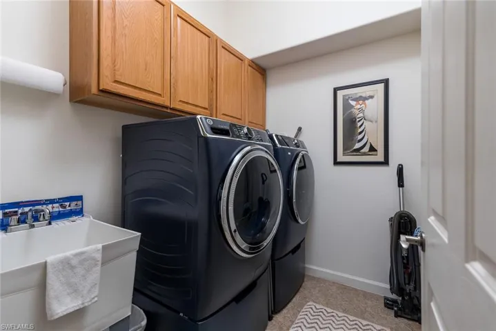 Clothes washing area with light colored carpet, a sink, baseboards, washer and dryer, and cabinet space