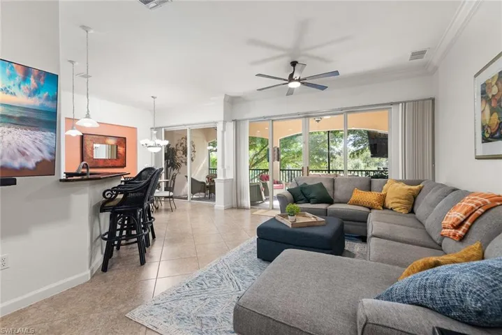 Living room featuring light tile patterned floors, a chandelier, ceiling fan, and crown molding