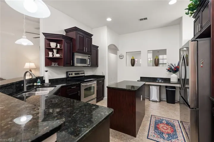 Kitchen with appliances with stainless steel finishes, dark stone countertops, decorative light fixtures, a center island, and open shelves