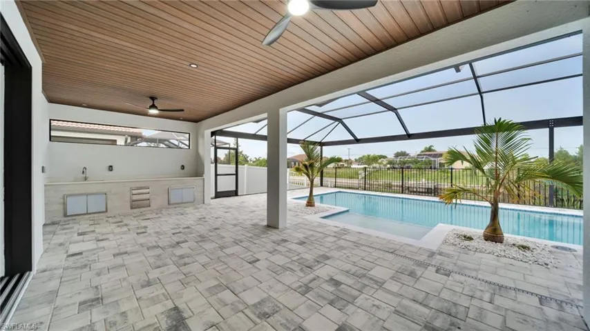 View of pool with a ceiling fan, an outdoor kitchen, a patio area, and glass enclosure