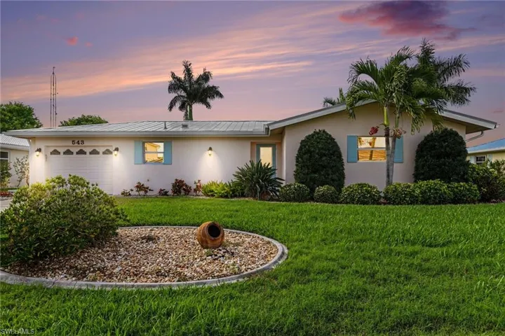 Ranch-style house with a garage, stucco siding, a lawn, and a metal roof