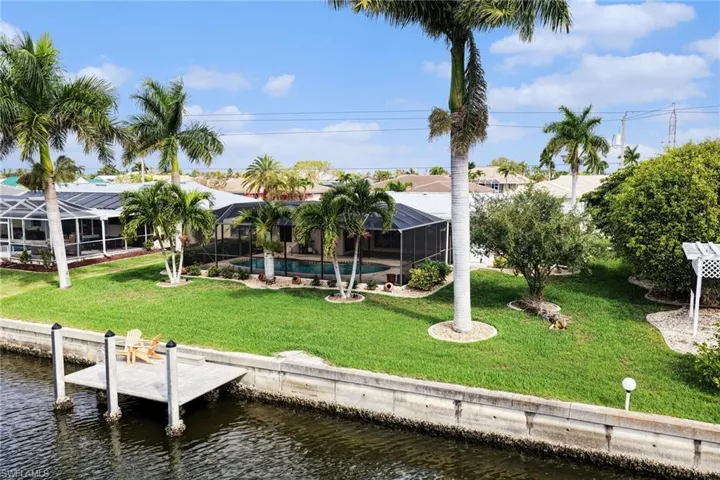 Back of property featuring a lawn, a water view, and glass enclosure