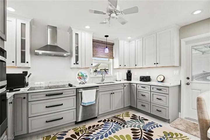 Kitchen featuring two tone cabinetry, stainless steel appliances, a ceiling fan, hanging light fixtures, and light stone counters