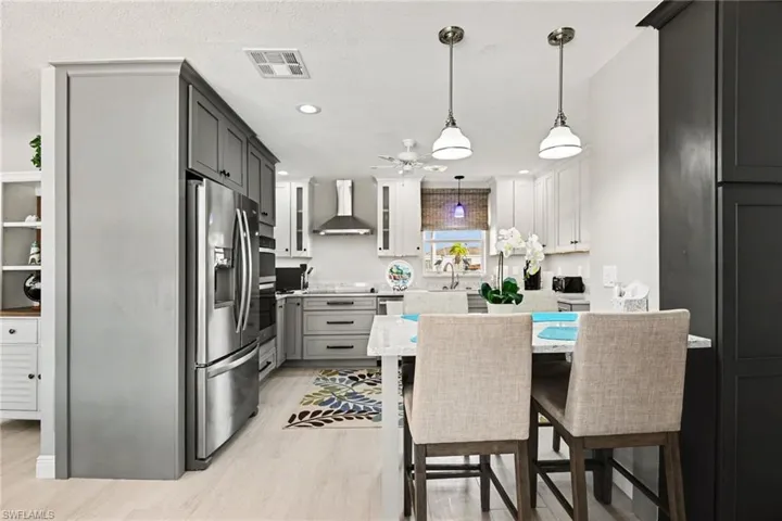 Kitchen with stainless steel appliances, a breakfast bar area, light stone counters, glass fronted cabinets, and decorative light fixtures