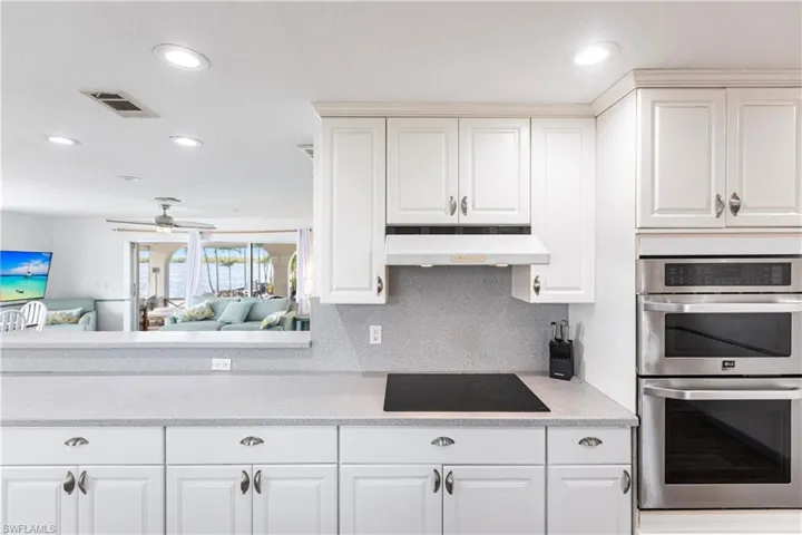 Kitchen featuring stainless steel double oven, under cabinet range hood, black electric cooktop, recessed lighting, and white cabinetry