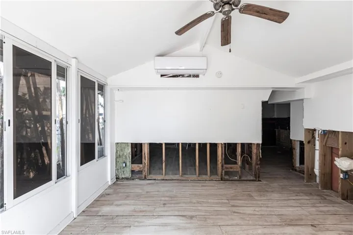 Empty room with an AC wall unit, wood finished floors, and ceiling fan