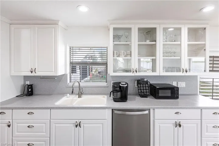 Kitchen featuring stainless steel dishwasher, black microwave, white cabinetry, glass insert cabinets, and light countertops