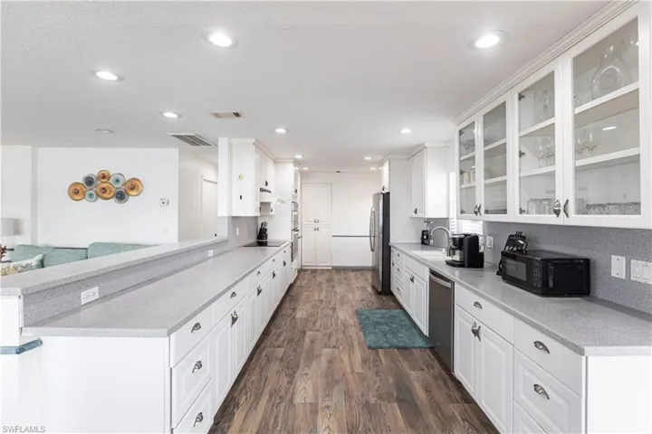 Kitchen with black appliances, dark wood-style flooring, white cabinetry, glass insert cabinets, and recessed lighting