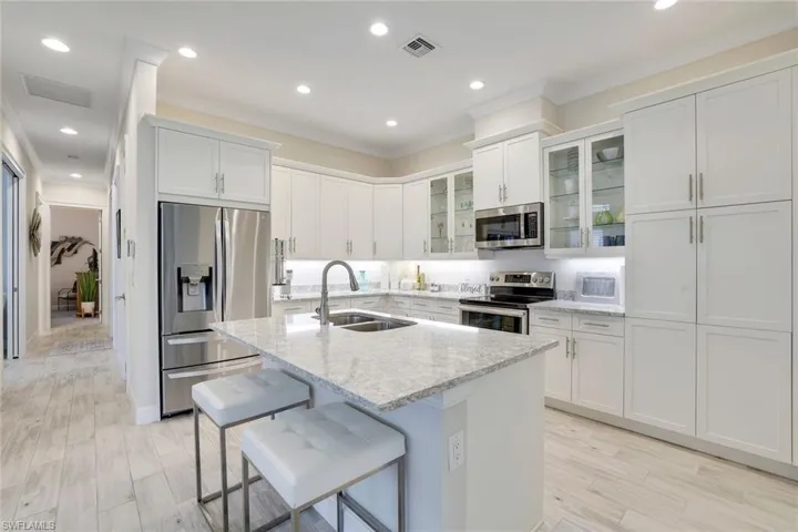 Kitchen featuring sink, stainless steel appliances, light stone counters, a center island with sink, and light wood-type flooring