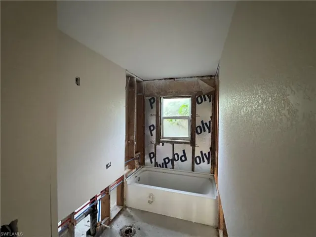 Bathroom under construction featuring a white bathtub, a window, and exposed wall studs
