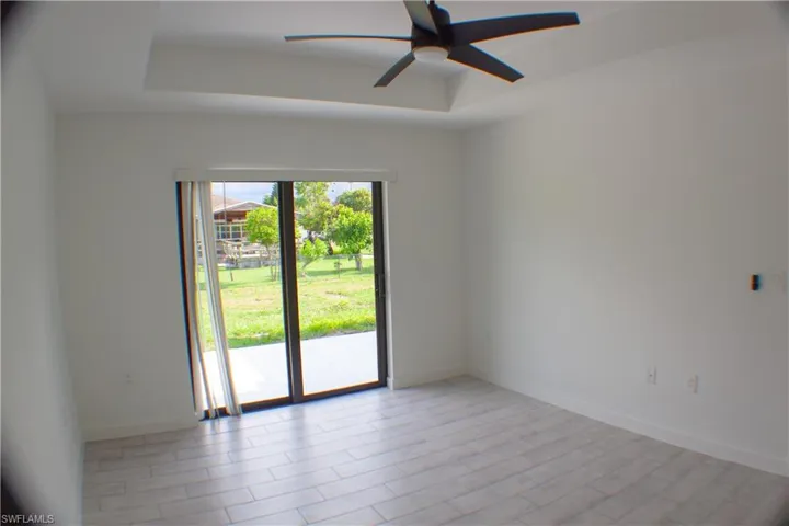 Spacious interior featuring light wood-finish flooring, a tray ceiling with a contemporary ceiling fan, and white baseboards