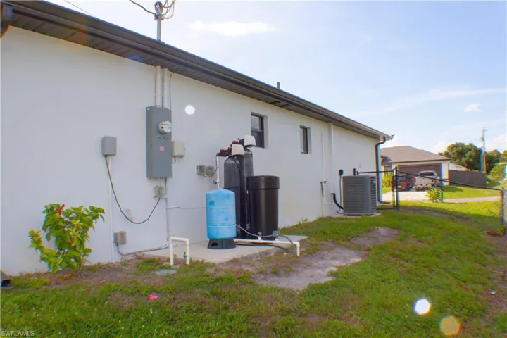 Exterior wall featuring a central electrical service panel, an air conditioning condenser unit, and a water treatment system on a concrete pad