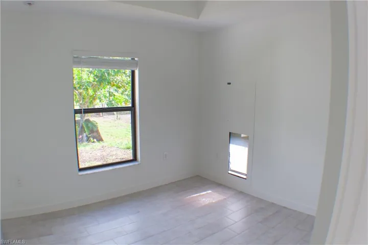 Bright room featuring a single window with outdoor views, light wood-finish flooring, and crisp white walls