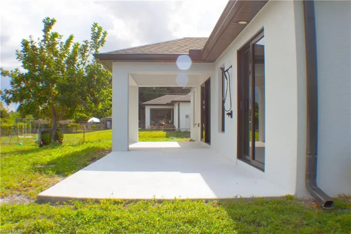 Expansive covered patio featuring a concrete surface, white stucco exterior, brown framed sliding glass doors, and an outdoor shower fixture