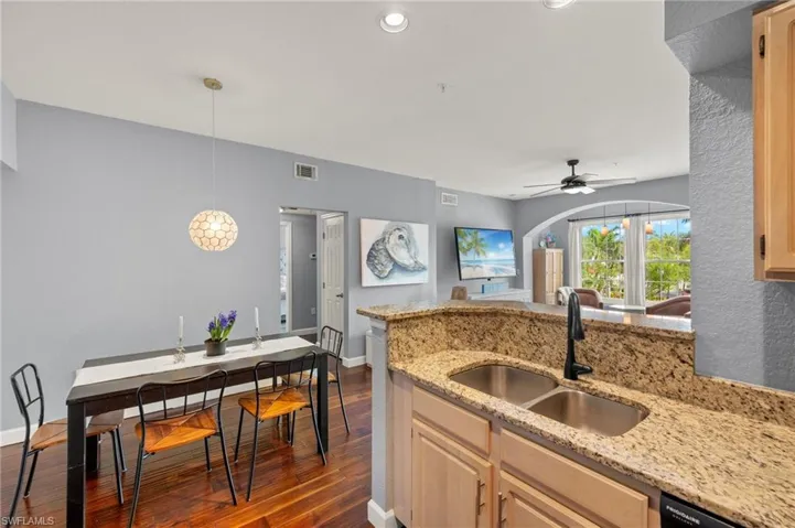 Kitchen with dark wood-style flooring, light stone countertops, a peninsula, a ceiling fan, and hanging light fixtures