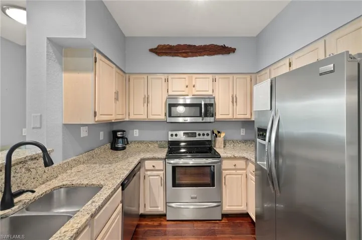 Kitchen with stainless steel appliances, light stone counters, dark wood-style floors, and light wood finish cabinets