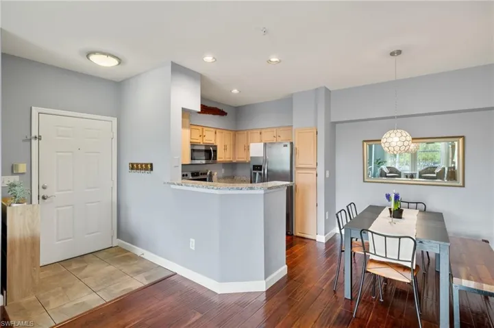 Kitchen with light wood finish cabinetry, a peninsula, stainless steel appliances, and dark wood-style flooring