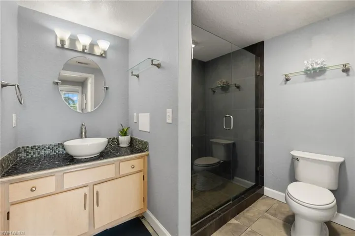 Bathroom featuring vanity, a textured ceiling, a shower stall, light tile patterned flooring, and a textured wall
