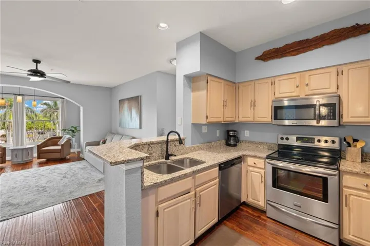 Kitchen featuring stainless steel appliances, open floor plan, dark wood-style flooring, light stone countertops, and recessed lighting