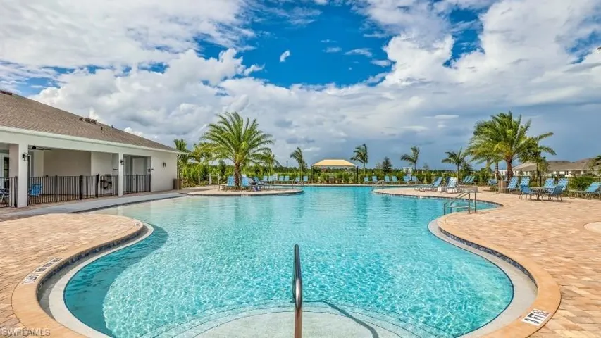 Expansive resort-style swimming pool featuring a curved design and a surrounding paver deck, lined with palm trees and lounge chairs