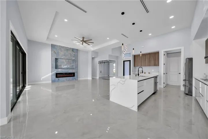 Kitchen with modern cabinets, hanging light fixtures, open floor plan, a tray ceiling, and a ceiling fan