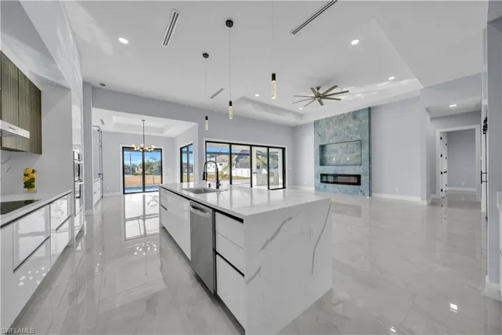 Kitchen with modern cabinets, a raised ceiling, pendant lighting, light stone counters, and open floor plan