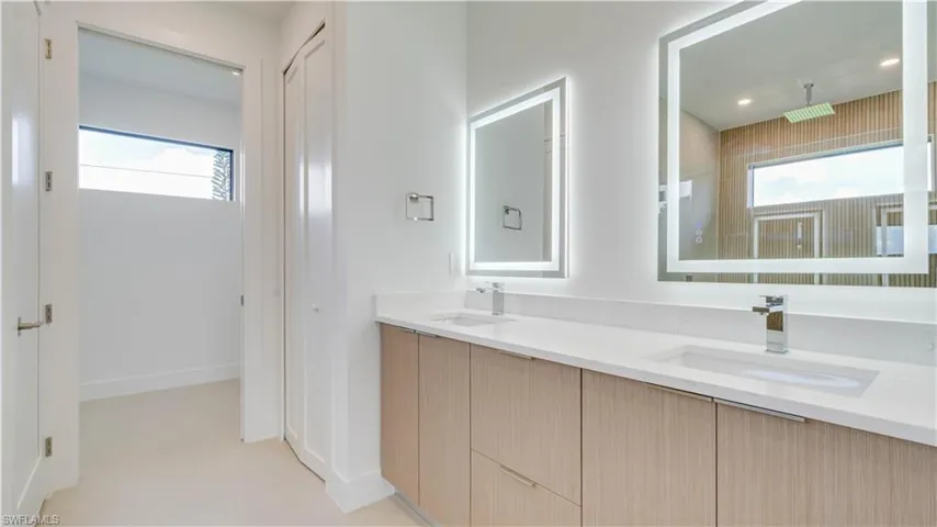Primary bathroom with double sink vanity, custom cabinetry, backlit mirrors, quartz countertops, and private toilet room.