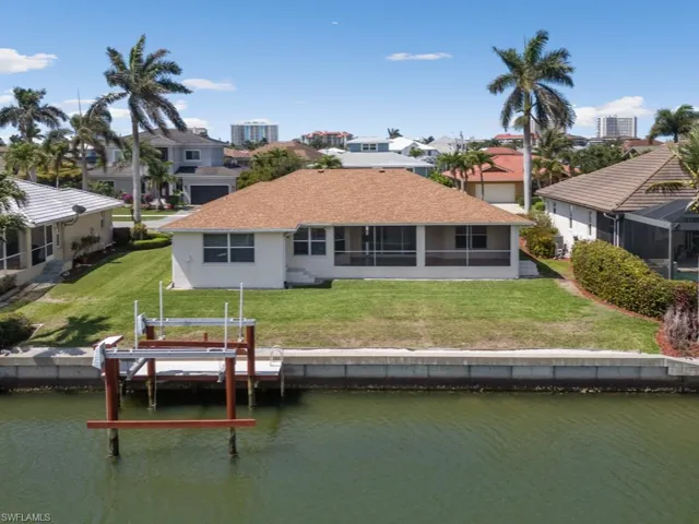 Back of house with a water view, boat lift, stucco siding, a shingled roof, and a yard