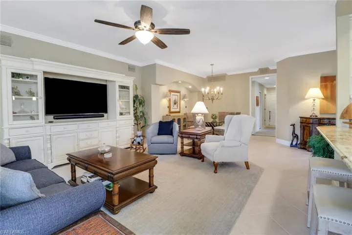 Living room with crown molding, ceiling fan with notable chandelier, and light tile patterned floors