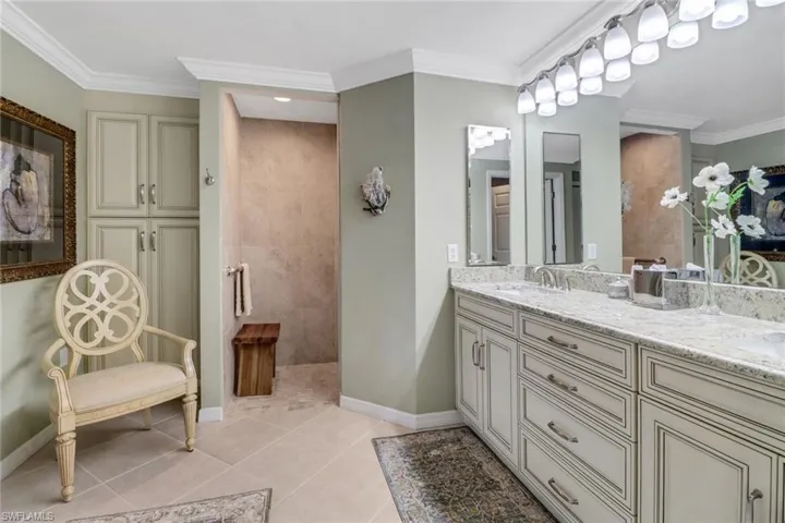 Bathroom with tiled shower, ornamental molding, tile patterned flooring, and vanity