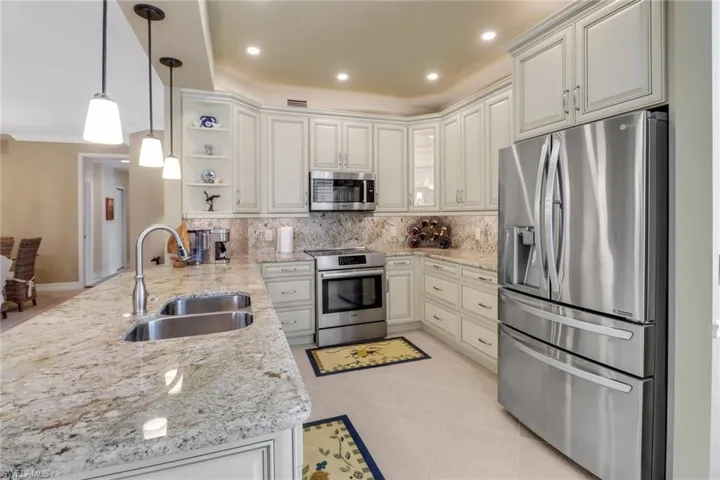 Kitchen with stainless steel appliances, sink, pendant lighting, and light stone counters