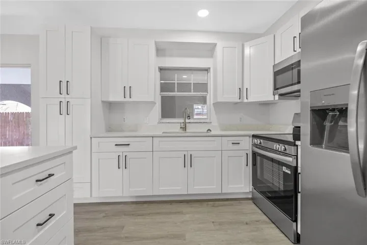 Kitchen featuring stainless steel appliances, white cabinetry, light wood-type flooring, light stone counters, and recessed lighting