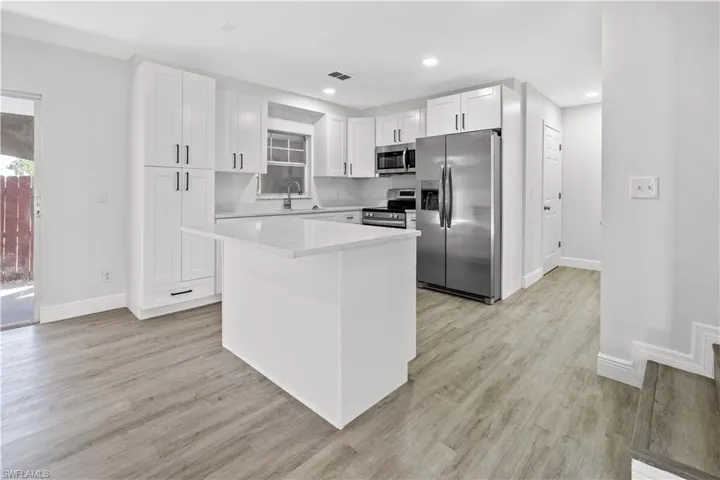 Kitchen featuring stainless steel appliances, white cabinets, a center island, light wood-type flooring, and light stone counters