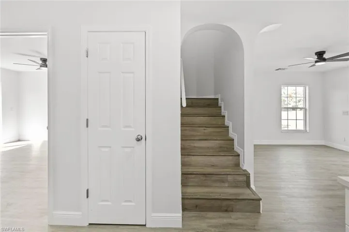 Stairway with a ceiling fan, arched walkways, and wood finished floors
