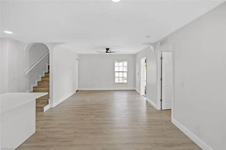 Unfurnished living room featuring arched walkways, light wood-type flooring, and ceiling fan