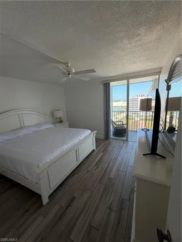 Bedroom featuring access to exterior, a ceiling fan, dark wood-type flooring, and a textured ceiling