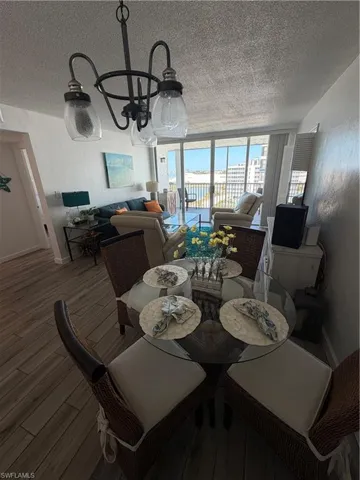 Dining space with a chandelier, wood finished floors, a textured wall, and a textured ceiling