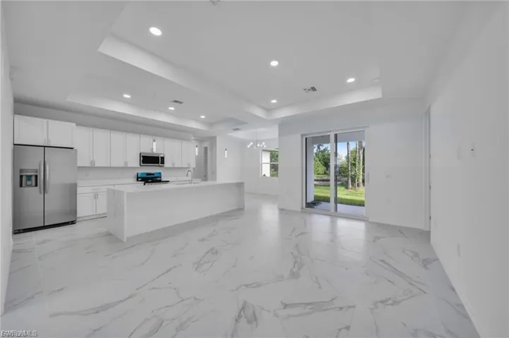 Kitchen with a raised ceiling, appliances with stainless steel finishes, open floor plan, white cabinets, and an island with sink