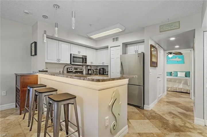 Kitchen featuring white cabinetry, a breakfast bar, stainless steel appliances, pendant lighting, and a peninsula