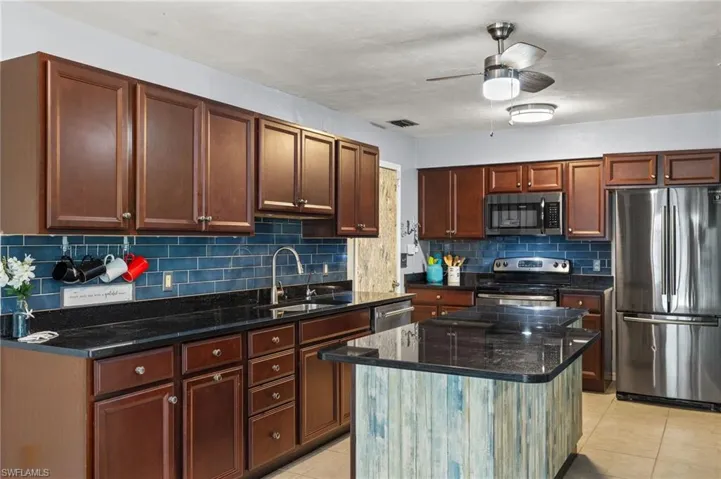 Kitchen with dark stone countertops, a center island, appliances with stainless steel finishes, ceiling fan, and decorative backsplash