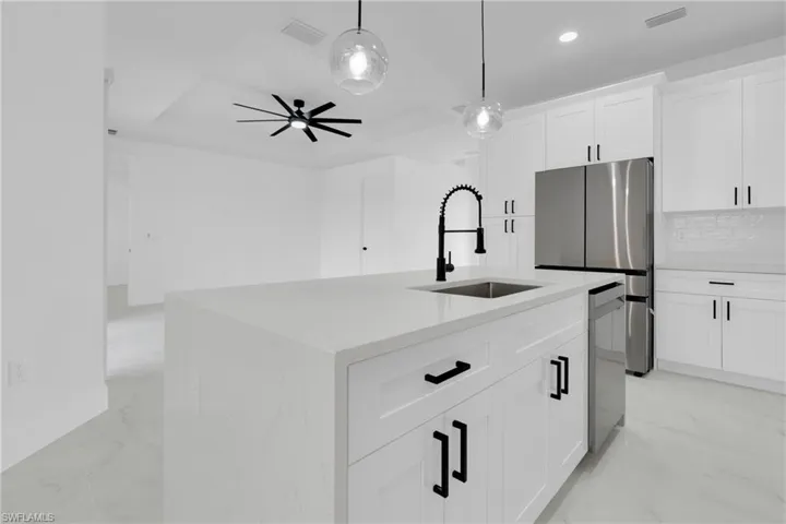 Kitchen featuring a center island with sink, white cabinets, light stone countertops, pendant lighting, and stainless steel appliances