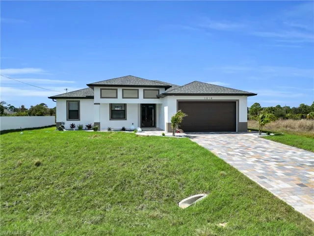 Prairie-style house with stucco siding, driveway, a shingled roof, and a front yard
