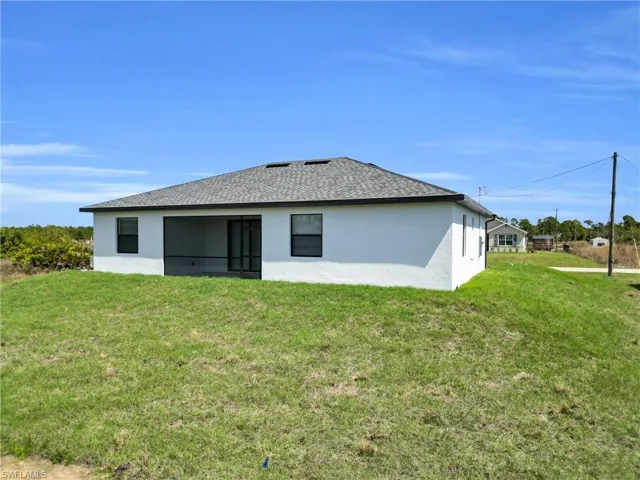 Rear view of property featuring stucco siding, a yard, and a shingled roof