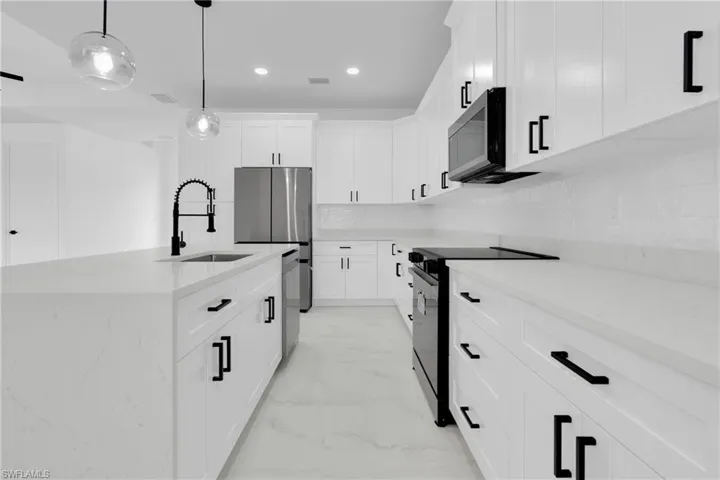 Kitchen with stainless steel appliances, light stone countertops, decorative light fixtures, white cabinetry, and a center island with sink