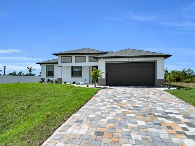 Prairie-style home featuring a front lawn, stucco siding, decorative driveway, and a garage