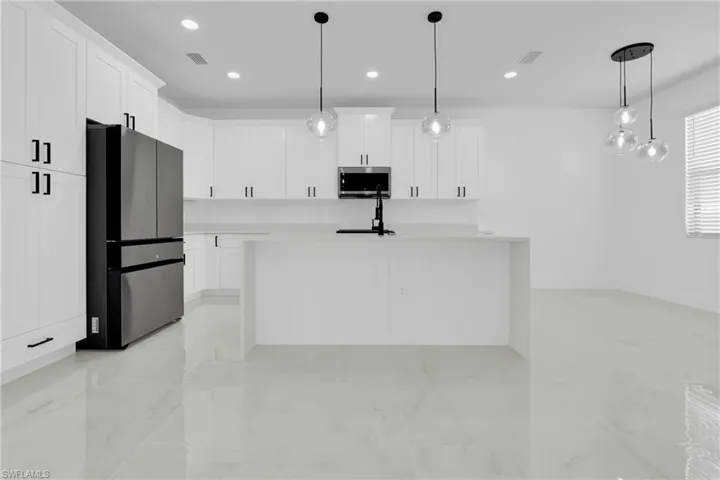 Kitchen featuring stainless steel appliances, white cabinets, an island with sink, light stone counters, and pendant lighting